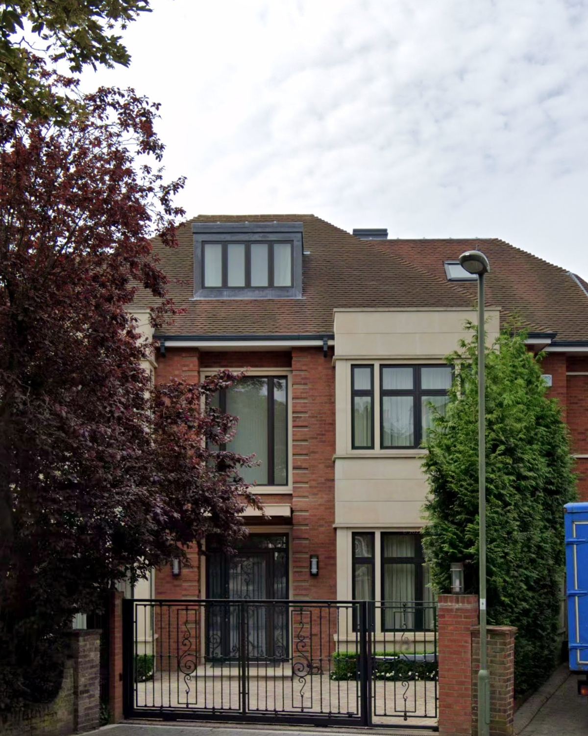 Portrait view of the façade: brick and pale stone, dormer window and wrought-iron gates
